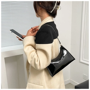 Glossy black patent leather baguette shoulder bag shown on model with minimalist interior