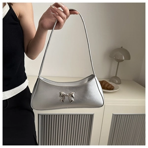 Detail of silver metallic underarm bag with decorative bow and sleek PU leather texture