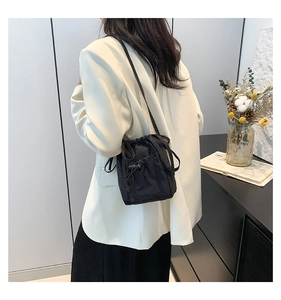 Detail showing a black nylon drawstring bucket bag on a model in a minimalist setting