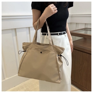 Close-up of khaki tote bag with magnetic clasp and drawstring detail on a model