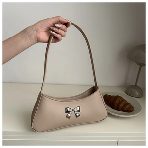 Detail of minimalist beige baguette bag featuring a metallic silver bow accent