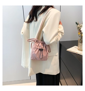 Detail view of pink drawstring bucket bag with pleated design worn as a crossbody