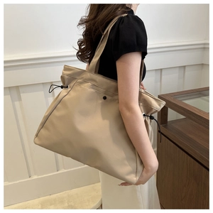 Side view of beige tote bag with drawstring detail shown on model in minimalist interior