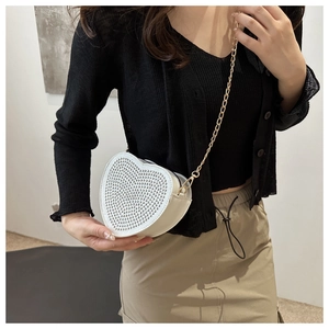Detail of white heart-shaped clutch bag with sparkling silver rhinestones and gold chain