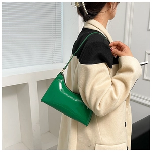 Close-up of bright green patent leather baguette bag worn over a beige coat