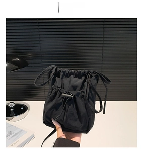 Detail view of the black nylon bucket bag featuring a drawstring closure and slim strap