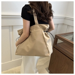 Detailed view of beige canvas tote bag with adjustable side drawstrings and wide shoulder strap