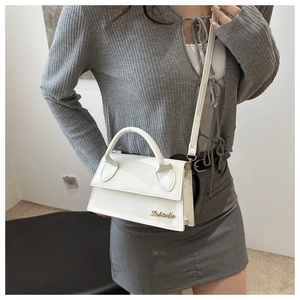 Close-up of a white glossy leather handbag with gold metal logo and round top handle