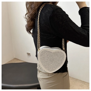 Detail of white heart-shaped bag with silver studs and elegant gold chain strap