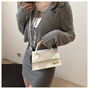 Detailed view of white mini crossbody bag with golden logo and slender leather strap