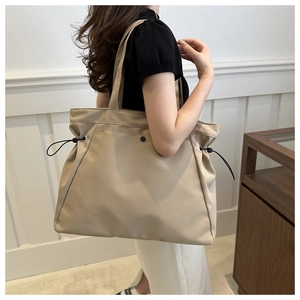 Detail of adjustable black drawstring on beige nylon tote bag shown on shoulder