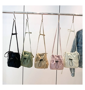 Detail of five nylon drawstring bucket bags in various colors hanging on a metal rack