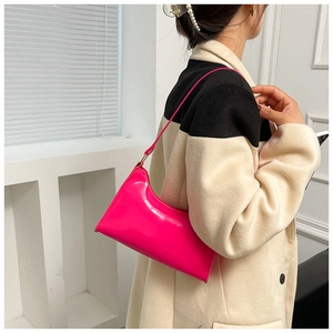 Close-up of bright fuchsia patent leather underarm bag shown on model in minimal coat