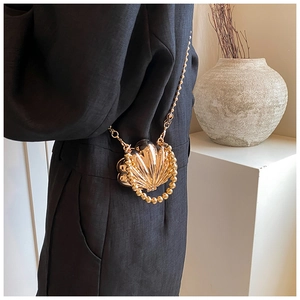 Detail of a mini gold shell bag with metallic texture and elegant beaded chain strap
