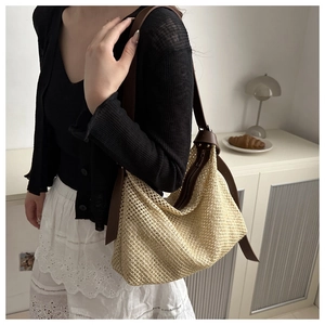 Detail of woven straw hobo bag with brown leather straps shown on a model in a bright room