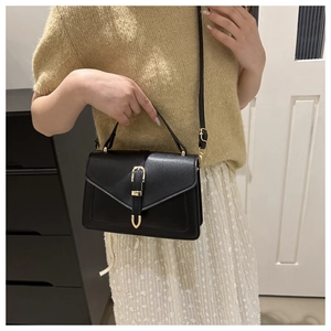 Fashionable black crossbody bag with gold buckle shown on a person for size reference