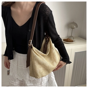 Detail view of woven straw shoulder bag with dark brown leather strap and metal buckle