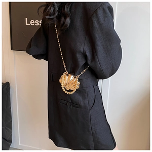 Detail of a golden seashell mini bag with chain strap worn against a black blazer suit