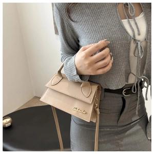 Detail view of a beige leather square crossbody bag with a gold Bobsaba metal logo