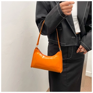 Detail view of glossy orange patent leather underarm bag worn on a shoulder