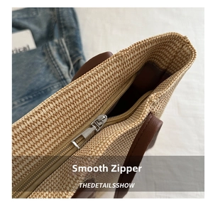 Detailed close-up of smooth metal zipper and brown leather handle on straw tote bag