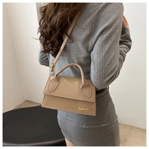 Model wearing a beige small crossbody bag with golden metal logo and adjustable strap