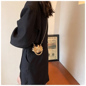 Side view of golden shell-shaped mini handbag with metallic chain and bead fringe