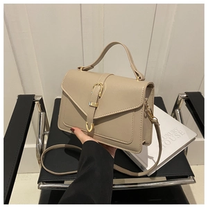Detail view of beige leather crossbody bag with metal buckle on a designer chair
