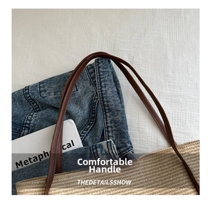 Detail of woven straw tote bag featuring brown leather handles and textured finish