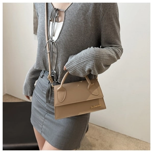 Beige trapezoid crossbody bag with gold logo shown with casual outfit for scale