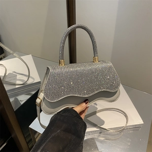 White crossbody bag with sequin wave flap and gold hardware held by a model