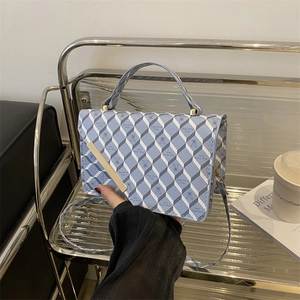 Blue and white quilted handbag with bear print and golden metal trim displayed in a lifestyle setting