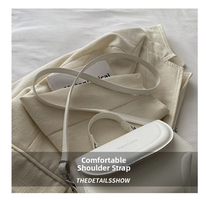 Detailansicht einer weißen Lederhandtasche auf einem beigen Blazer mit schmalem Schultergurt