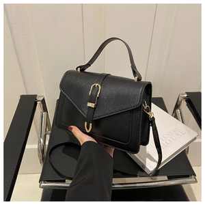 Close-up of matte black small square bag with golden U-shaped buckle and fine leather strap