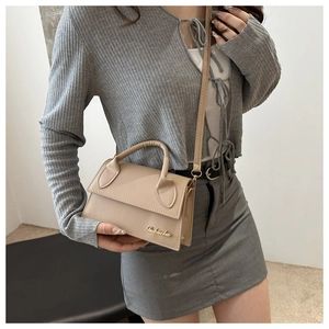 Dettaglio della borsa a tracolla in pelle beige con logo dorato e manico superiore