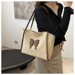 Detail of summer straw tote bag featuring leather butterfly patch and long shoulder straps