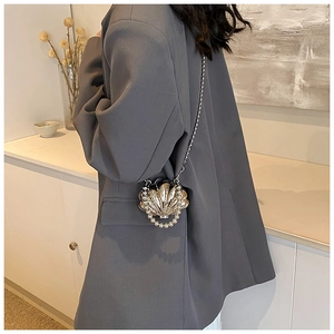 Detail of a silver shell-shaped mini bag with metallic texture and pearl handle strap