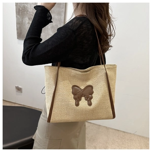 Detail of woven straw tote bag featuring a brown leather butterfly applique and slim shoulder straps