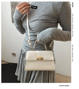 Close-up of white crocodile pattern handbag with gold clasp and adjustable strap
