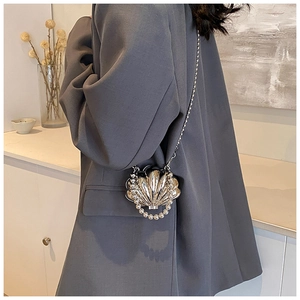 Close-up of silver shell-shaped mini bag with pearl handle and metal chain on a model