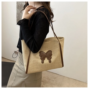 Close-up of a woven straw tote bag featuring a leather butterfly patch and shoulder straps