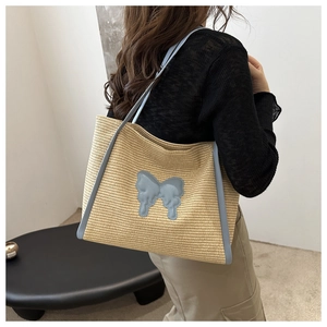 Detail of woven straw tote bag with light blue bow and leather handles on model