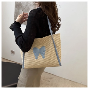 Close-up of a woven straw tote bag with light blue leather straps and butterfly patch