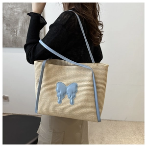 Detail of woven straw tote bag with 3D blue butterfly applique and slim shoulder strap