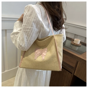 Detail of handwoven straw tote bag with pink butterfly patch and shoulder strap on model