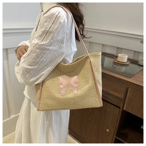 Detail of summer straw tote bag featuring a large pink bow and leather handles on model