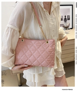 Pink quilted tote bag with gold chain strap worn by model in a cozy lifestyle setting