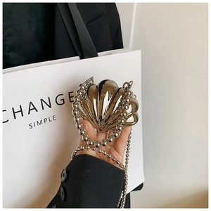 Detail of silver shell-shaped evening clutch bag with glossy metallic finish and ball chain