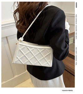Détail d'un sac baguette blanc matelassé avec bandoulière nouée sur un blazer noir chic