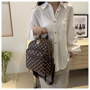 Side view of checkered backpack with gold zippers and leather handle in a minimalist setting